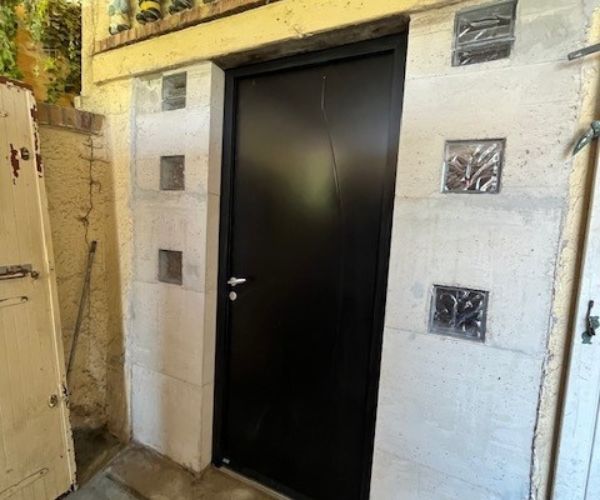 Mur en béton armé blanc avec briques de verre et porte d’entrée en acier noir posée en tunnel